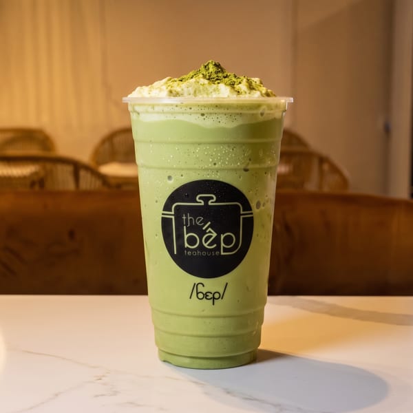 Large green matcha frappe with whipped cream and matcha powder, featuring the bép teahouse logo.