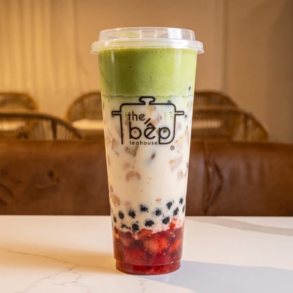 Layered drink from The Bep Teahouse with matcha foam, milk, boba, and strawberries on a white table.