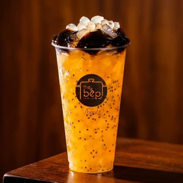 Vibrant orange drink with basil seeds, dark jelly, and clear toppings in a The Bep Teahouse cup.