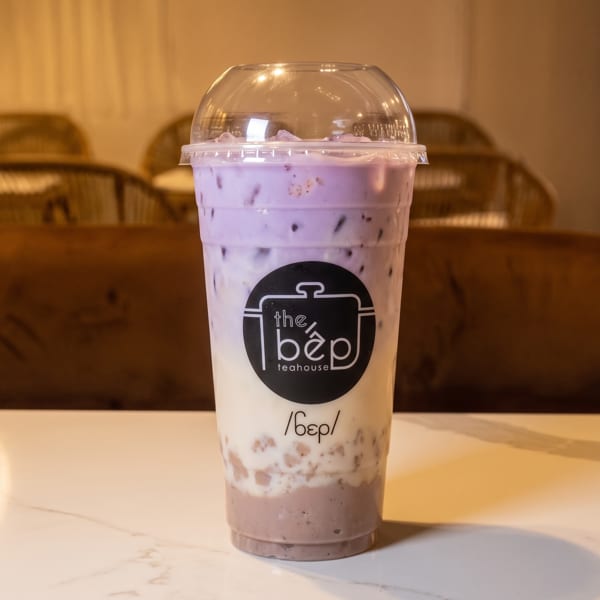 Layered purple and white drink from The Bep Teahouse in a plastic cup on a white table.