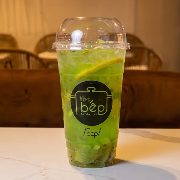 Green kiwi and lemon drink in a branded "the bep teahouse" cup on a white marble table.